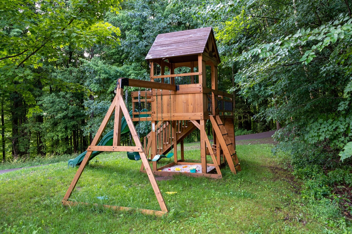 A wooden playset with a slide, ladder, and platform in a grassy backyard