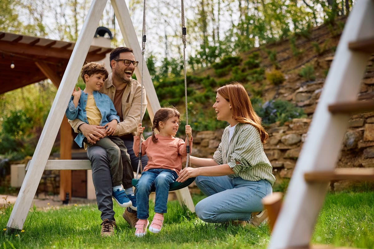 Happy parents and children laughing and having fun while swinging in the backyard