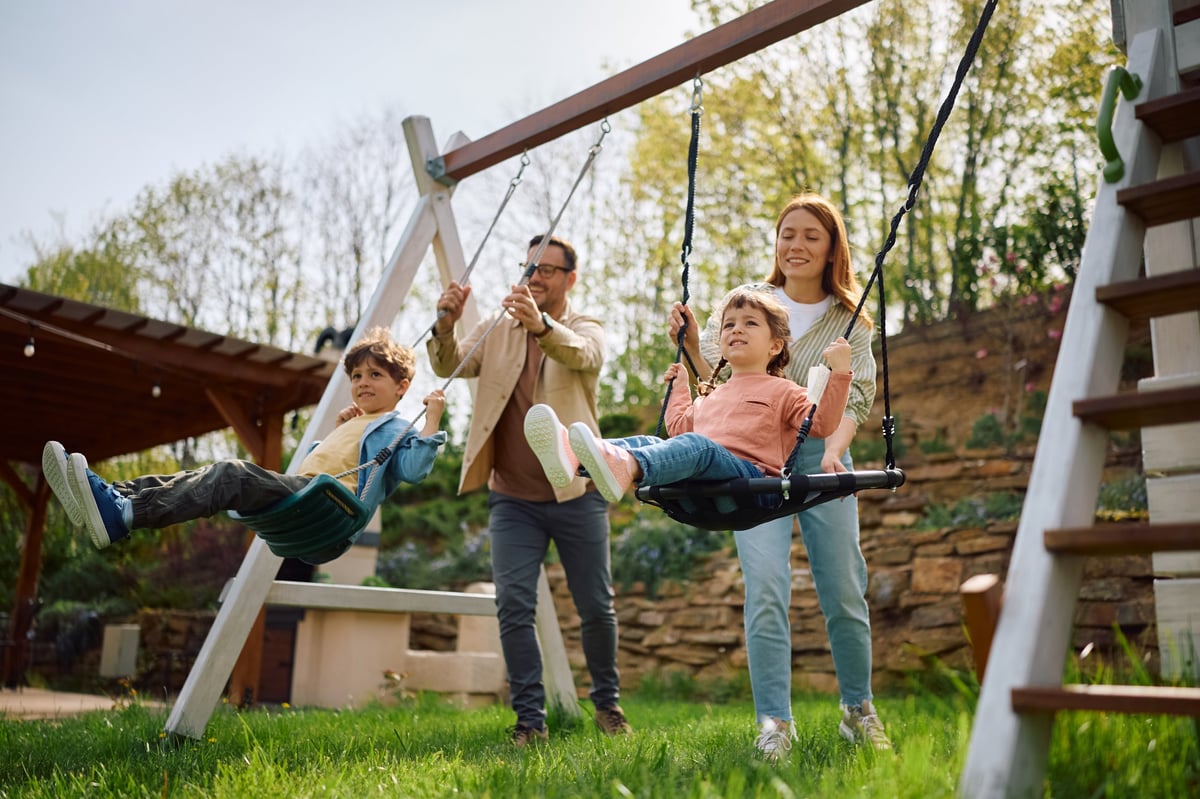 Happy kids having fun while being pushed on a swing by their parents