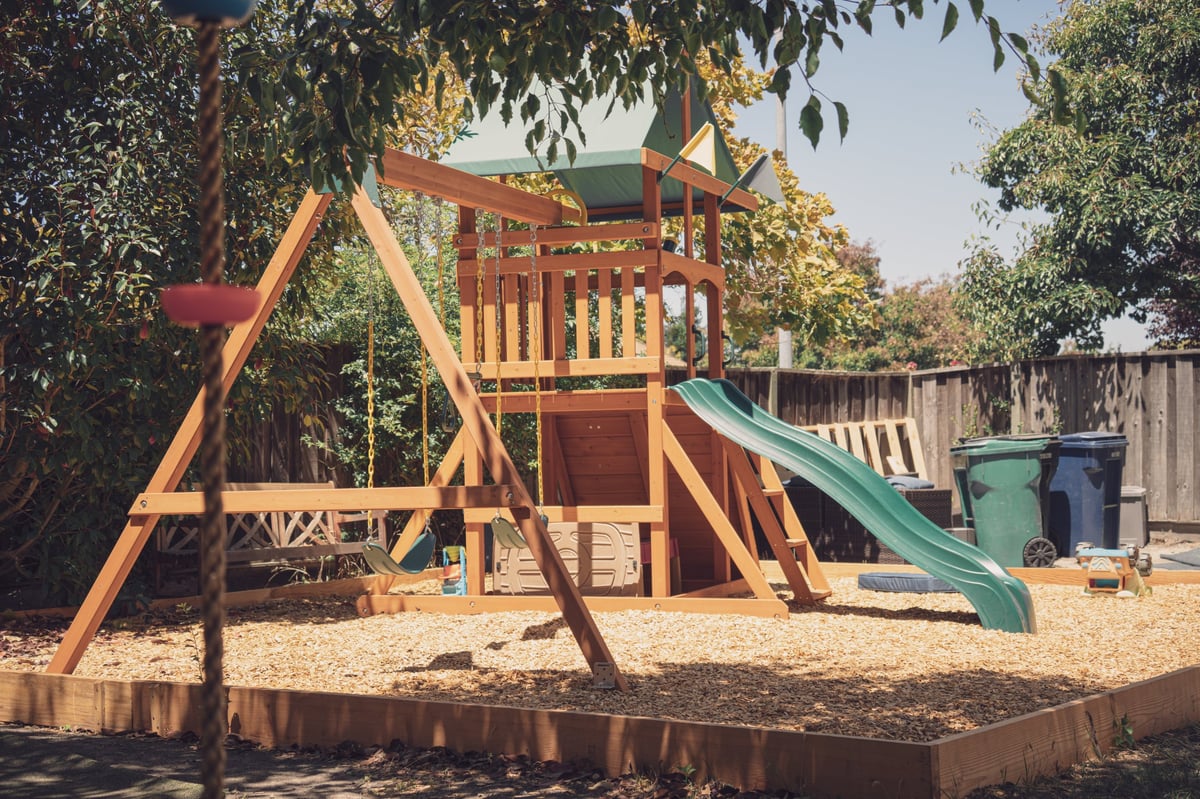 A finished wooden playset with slide and swings in a backyard